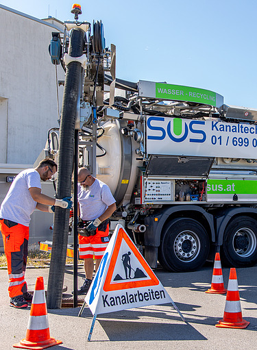 Großes Einsatzfahrzeug der Firma SUS bei Arbeiten im Straßenbereich mit Absperrungen, Leitkegeln und Warnschild.